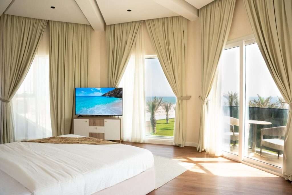 غرفة نوم بتلفاز ونوافذ واسعة تطل على الحديقة – Bedroom with TV and large windows overlooking the garden