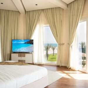 غرفة نوم بتلفاز ونوافذ واسعة تطل على الحديقة – Bedroom with TV and large windows overlooking the garden